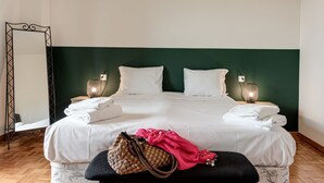 A neatly made bed with white linens, two bedside lamps, a mirror, and a bench with a woven bag and pink cloth. - Balcone sul Verde - Sweet Dreams in Florence (Firenze)