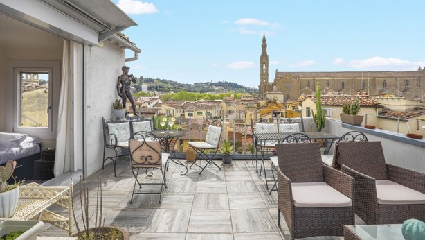A rooftop terrace with wicker furniture, a statue, and a view of a historic building with a tower. - Dante - Sweet Dreams in Florence (Firenze)