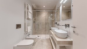 A modern bathroom with a bathtub, two sinks, a toilet, and a glass shower enclosure.