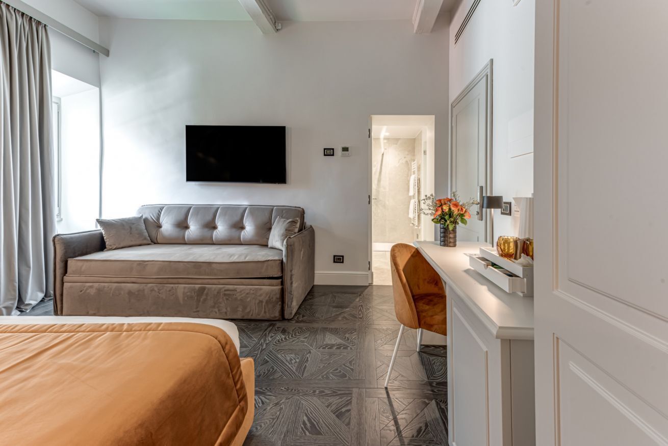 Une chambre d’hôtel équipée d’un lit, d’un canapé, d’un bureau avec un miroir et d’un téléviseur fixé au mur.