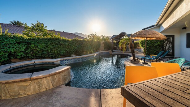 Un espace piscine doté d’un jacuzzi, de chaises longues et d’un parasol en chaume.