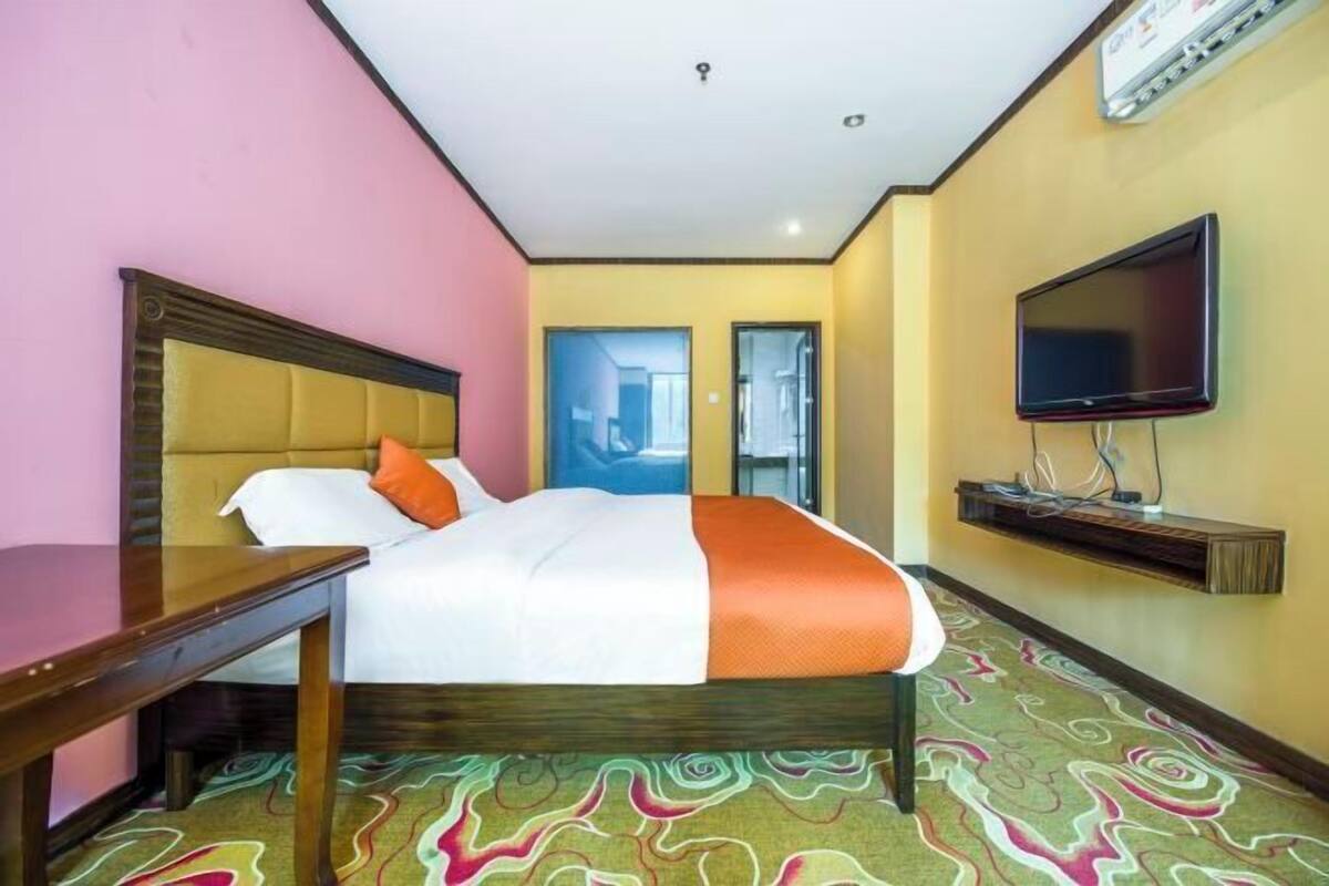 Una camera d'albergo con un letto, una televisione, una scrivania e un tappeto decorato.