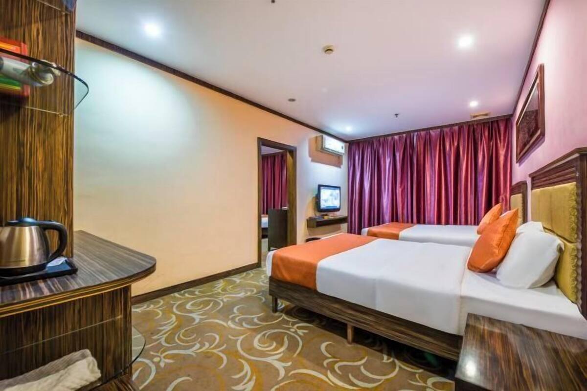 Una camera d'albergo con due letti, una scrivania con un bollitore, una televisione e una moquette fantasia.
