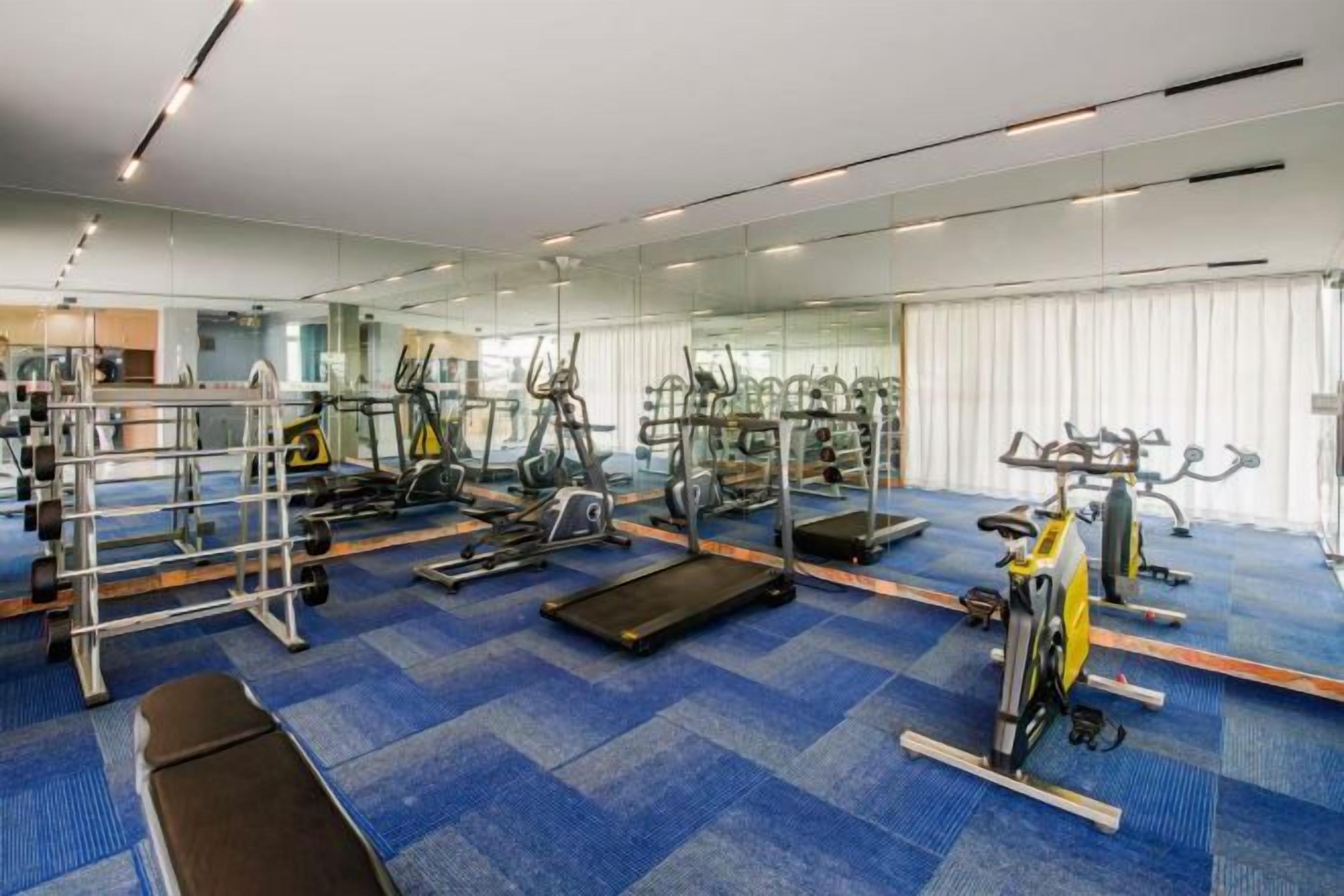 Ein Fitnessstudio mit Trainingsgeräten, Spiegeln und einem blau teppichbelagten Boden.