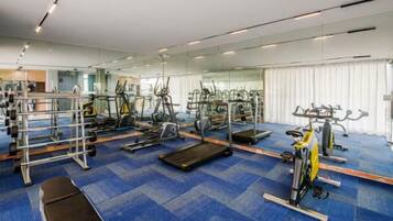 Ein Fitnessstudio mit Trainingsgeräten, Spiegeln und einem blau teppichbelagten Boden.