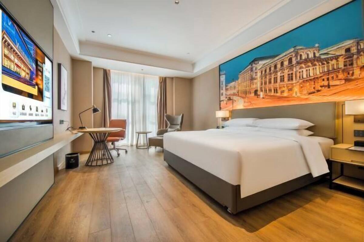 Camera d'albergo con un letto, una scrivania, una sedia, una televisione e un'ampia finestra.