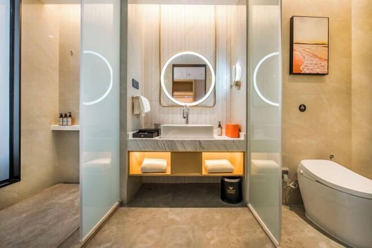Un bagno moderno con divisorio in vetro, uno specchio rotondo, un lavandino bianco e un water.