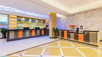 A hotel reception area with a marble wall, a reception desk, and a digital screen.