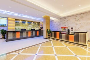 Zona de recepción de un hotel con pared de mármol, mostrador de recepción y pantalla digital.