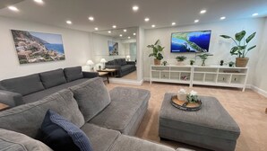 Een moderne woonkamer met grijze banken, een salontafel en een aan de muur bevestigde televisie.