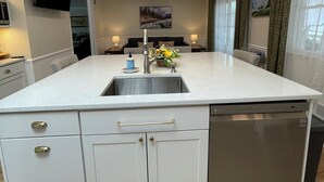 Een moderne keuken met een centraal eiland, roestvrijstalen apparatuur, hanglampen en een flatscreen televisie aan de muur.