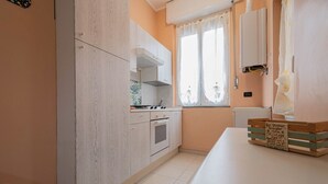Una cocina con armarios blancos, estufa y ventana con cortinas traslúcidas.