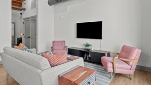 A modern living room with a grey sofa, two patterned armchairs, a wooden coffee table, and a flat-screen TV mounted on the wall. - Riverfront DWTN Loft W/D Gated Parking (St. Louis)
