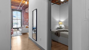 A modern, well-lit room with a large mirror, a bed with a bedside table, and a view through a window. - Riverfront DWTN Loft W/D Gated Parking (St. Louis)