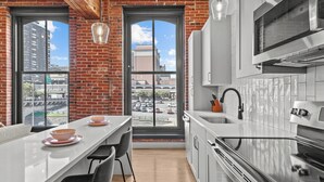 A modern kitchen with a large island, white cabinets, and a view of the city through large windows. - Riverfront DWTN Loft W/D Gated Parking (St. Louis)