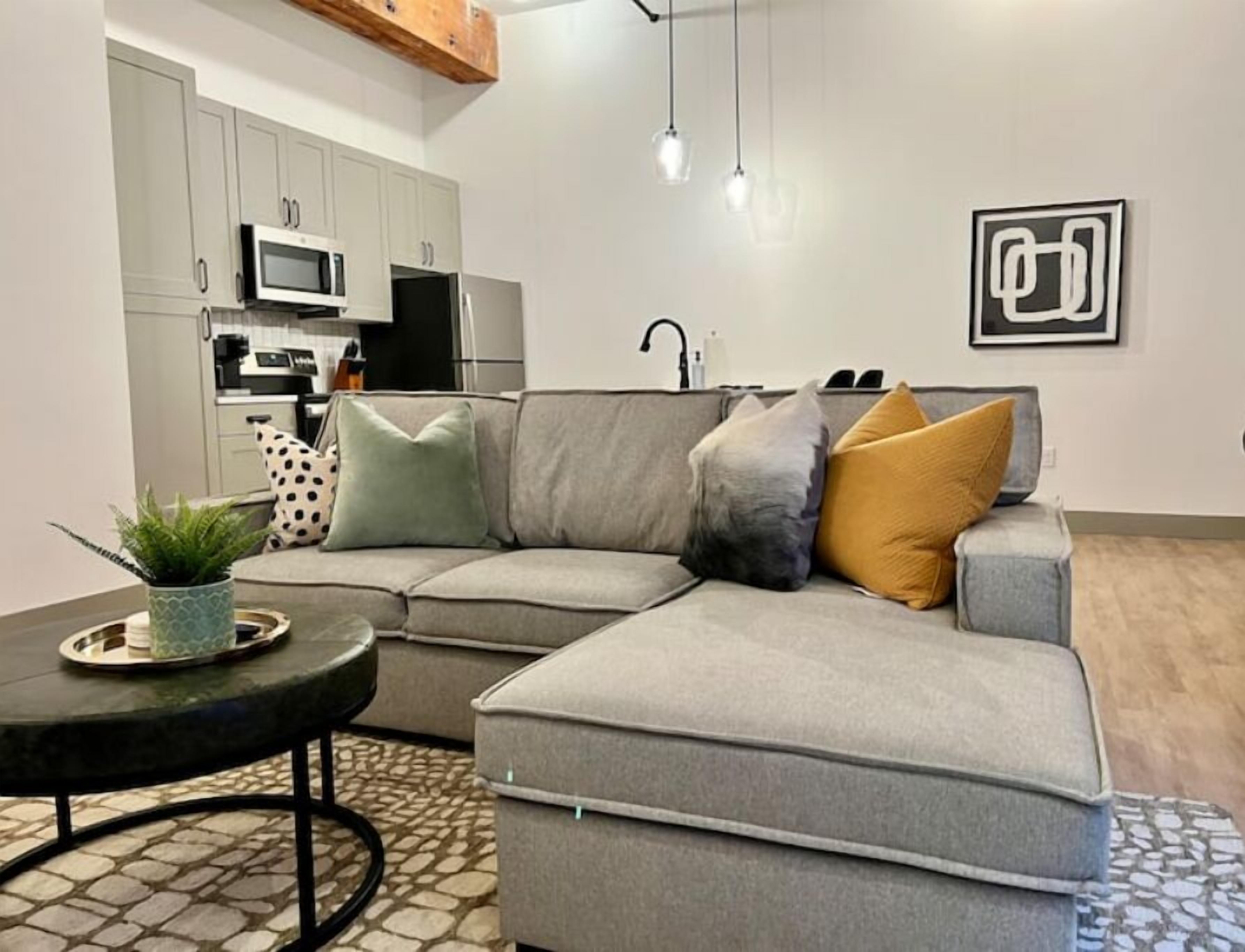 A modern living room with a grey sectional sofa, a small round table, and a potted plant.