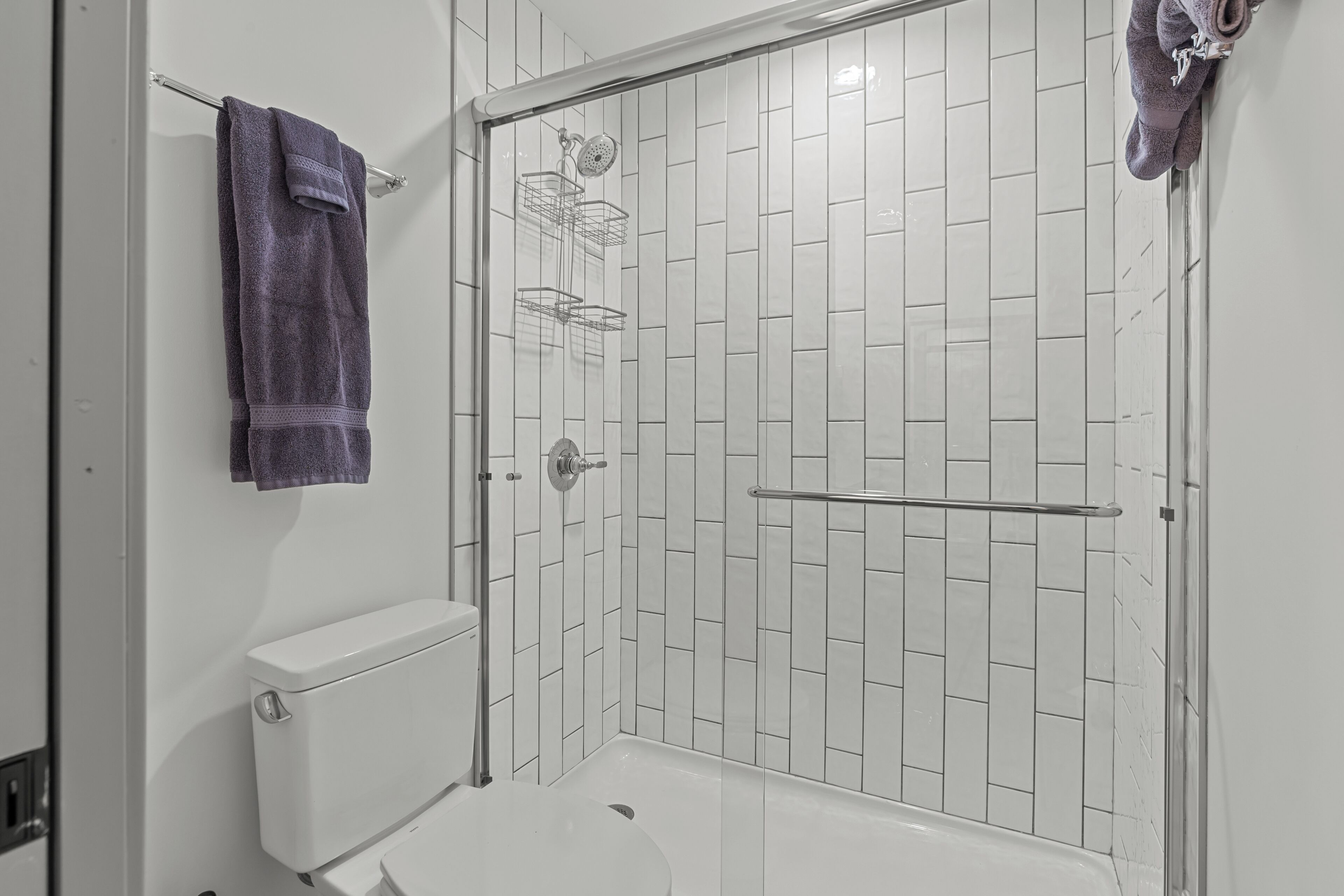 Une salle de bain avec des toilettes blanches, une douche dotée d’une porte en verre et un porte-serviettes.