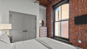 Un dormitorio con una cama grande, un aparador, un espejo y un televisor montado en una pared de ladrillo.