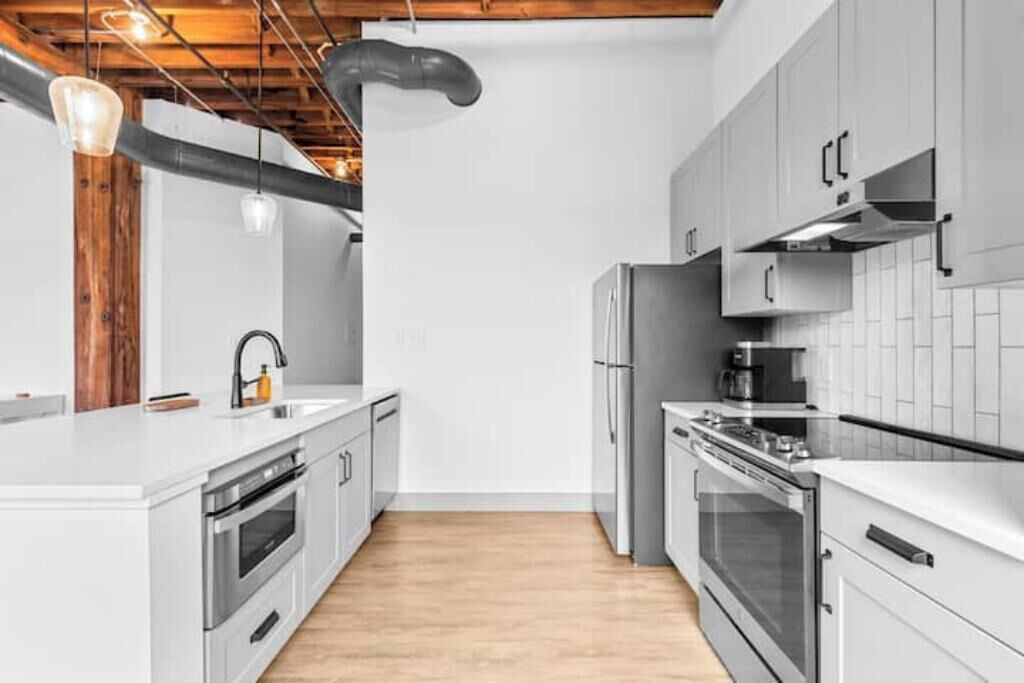 A modern kitchen with white cabinets, stainless steel appliances, and a wooden ceiling.