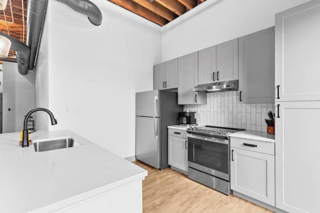 A modern kitchen with white cabinets, stainless steel appliances, and a wooden ceiling.