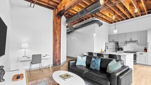 Ein moderner Wohnraum mit einem schwarzen Ledersofa, einem kleinen weißen Tisch und einer Küchenzeile mit weißen Schränken und einem Edelstahlkühlschrank.