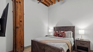 A bedroom with a wooden bed frame, a nightstand, and a wall-mounted TV. - Downtown Loft on Riverfront Next to Arch & Convention Center (St. Louis)