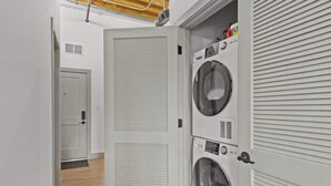 A laundry room with two stacked washing machines, a closed door, and a wooden floor. - Downtown Loft on Riverfront Next to Arch & Convention Center (St. Louis)