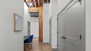Un pasillo con techo de madera, una obra enmarcada en la pared, una silla azul y puertas grises.
