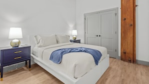 Un dormitorio con cama, dos mesitas de noche con lámparas, un armario y una puerta de madera.