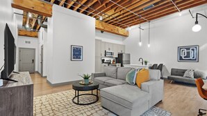 A modern living room with a gray sofa, a coffee table, and a kitchen in the background. - Riverfront Loft Steps from Arch & Convention Center - Walk to Stadium (St. Louis)