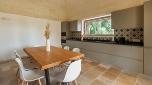 A modern kitchen with a wooden dining table and white chairs, a window with a view of greenery, and patterned backsplash tiles. - Villa Cinera - Luxury Villa with private pool (Ostuni)
