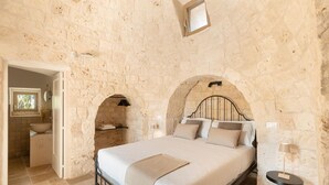 A bedroom with a stone wall, a bed with a headboard, a bedside table, and a small window. - Villa Cinera - Luxury Villa with private pool (Ostuni)