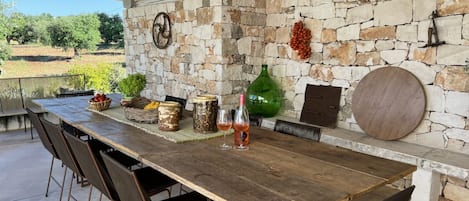 Un área de comedor al aire libre rústica con un muro de piedra, una mesa y sillas de madera.