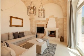 Un salon avec une cheminée en pierre, un canapé, une table basse et des luminaires suspendus.