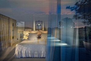 Une chambre à coucher avec un lit, une table de chevet, une lampe et une fenêtre donnant sur l’extérieur.