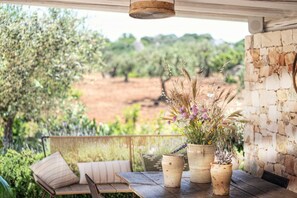 Un espace extérieur aménagé avec une table et des chaises, un mur en pierre rustique et une vue sur un jardin et des arbres.