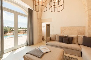 A spacious living room with a large sliding glass door leading to a pool area, a beige sofa with multiple cushions, and a modern pendant light fixture.