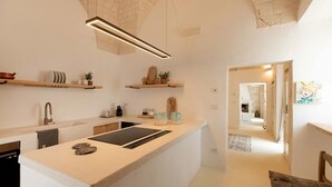 A modern kitchen with a central island, built-in appliances, and decorative items on floating shelves.