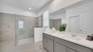 Un baño moderno con ducha envuelta en vidrio, un tocador amplio con espejo y una planta en maceta.