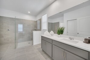 Une salle de bain moderne avec une douche à parois de verre, un grand meuble-lavabo avec un miroir et une plante en pot.