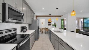 A modern kitchen with stainless steel appliances, a large island, and pendant lighting. - Private Theater! Minions Gameroom! MARIO Bunks! Close to Disney! (Kissimmee)