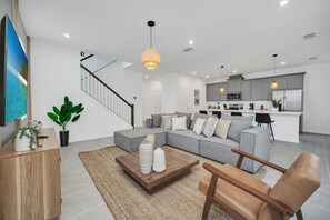 A modern living room with a sectional sofa, a coffee table, and a staircase leading to an upper floor.