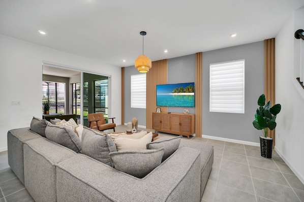 A modern living room with a grey sectional sofa, a wooden cabinet, and a large flat-screen TV.