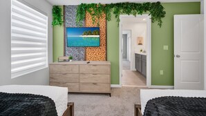 Un dormitorio con una cama grande, un aparador, un televisor montado en la pared con papel tapiz tropical y vistas a la habitación contigua.