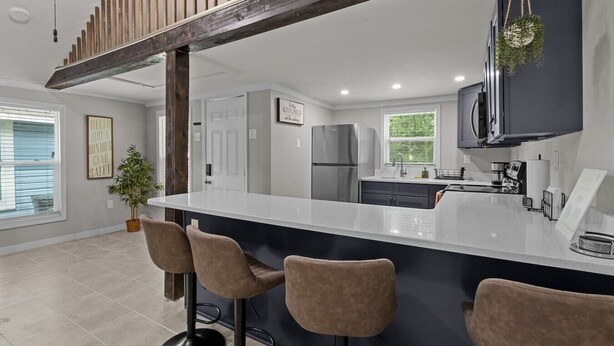 A modern kitchen with a large island, bar stools, a refrigerator, and a hanging plant.