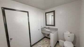 Un baño con puerta, un lavabo con espejo, inodoro y un cubo de basura.