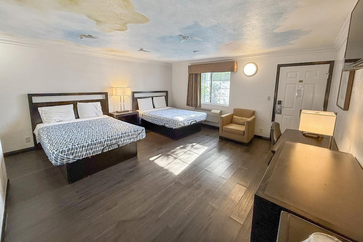 A hotel room with two beds, a chair, a desk, and a ceiling mural.