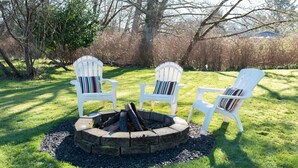 A fire pit with three Adirondack chairs around it, set in a grassy outdoor area with trees in the background. - Cozy and Stylish-Walk To The Beach - Sleeps 5 (Grayland)