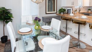 A modern kitchen with a glass dining table, white chairs, and a hanging light fixture. - Cozy and Stylish-Walk To The Beach - Sleeps 5 (Grayland)