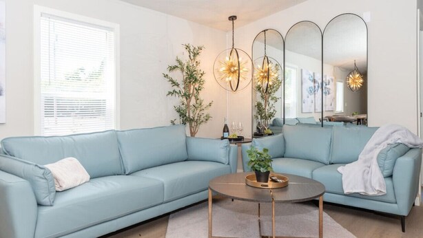 A living room with a light blue sofa, a round coffee table, and a mirror with three lights. - Dragonfly Beach Retreat (Grayland)